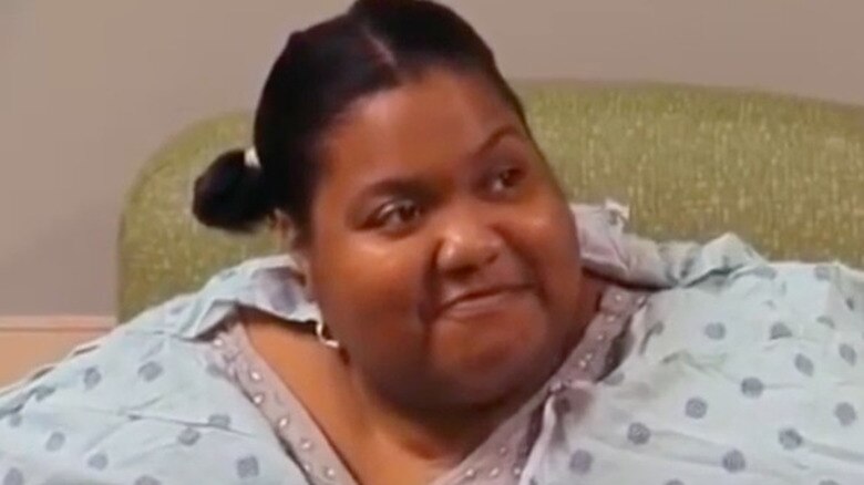 Participante sorrir enquanto está sentada olhando para a câmera. Ela veste um grande vestido de bolinhas