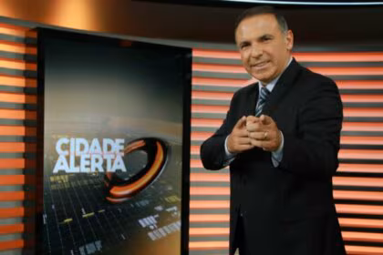 Reinaldo Gottino sorridente, apontando o dedo pra frente, no cenário do Cidade Alerta