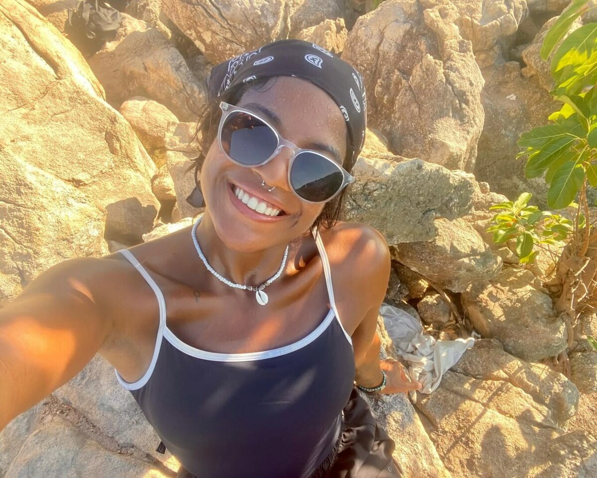 Juliana Marins sorrindo com óculos de sol próximo a umas pedras