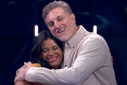 Luciano Huck abraça Eliza no palco do Quem Quer Ser Um Milionário no Domingão. Ela está sorrindo