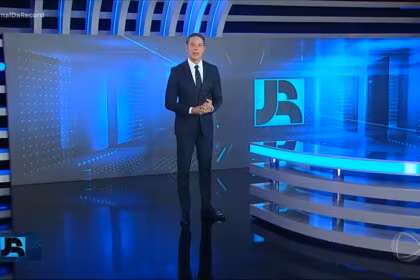 Sergio Aguiar em pé no centro do cenário do jornal da Record vestindo terno preto alguns dias antes de sua demissão. Ele está com semblante sério.