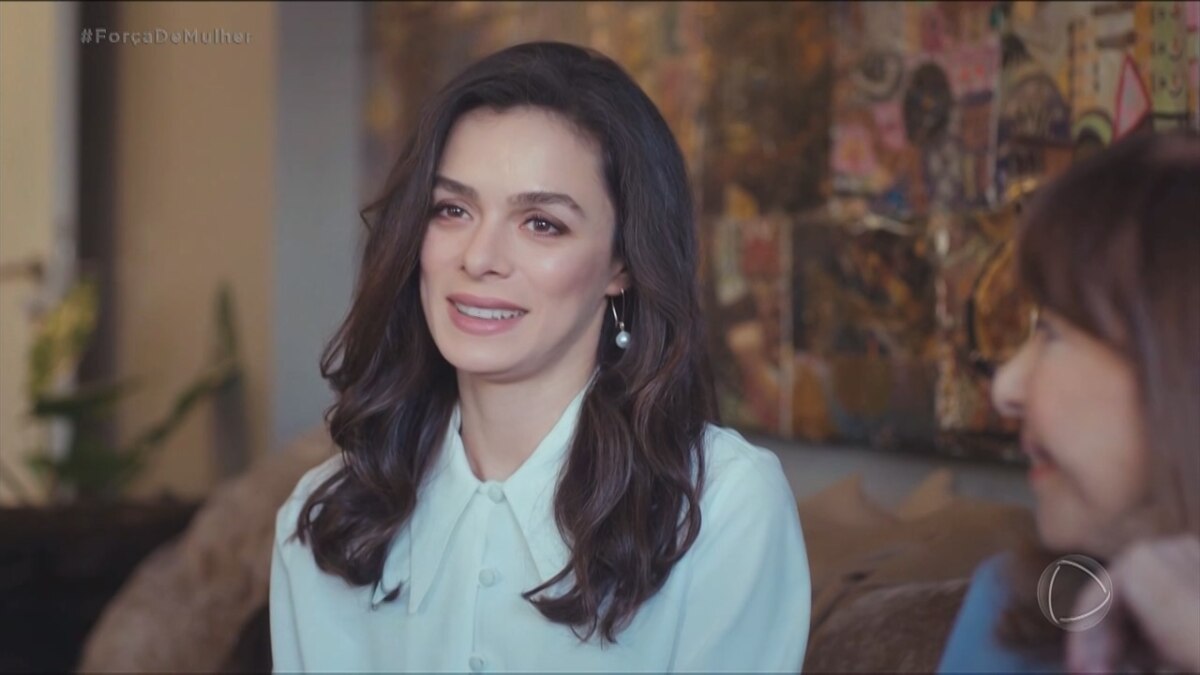 Bahar com roupas finas e sorridente. Ela está sentada em um sofá em cena dos últimos capítulos da novela Força de Mulher