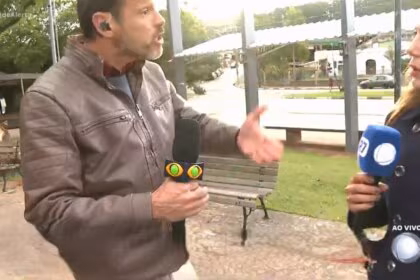 Lucas Martins com o microfone da Band nas mãos gritando com a repórter Grace Abdou que segura o microfone da RECORD
