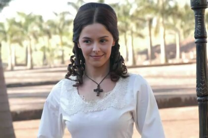 Bianca Rinaldi de vestido branco e com um colar de cruz no pescoço em campo nos bastidores de A Escrava Isaura