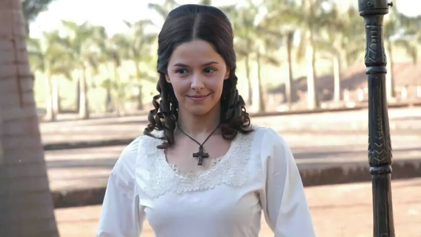 Bianca Rinaldi de vestido branco e com um colar de cruz no pescoço em campo nos bastidores de A Escrava Isaura