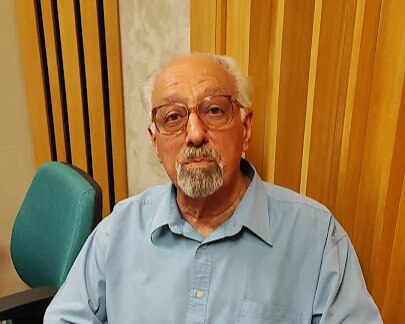 Hélio Vaccari em um estúdio de gravação. Ele usa óculos de grau e camisa azul social