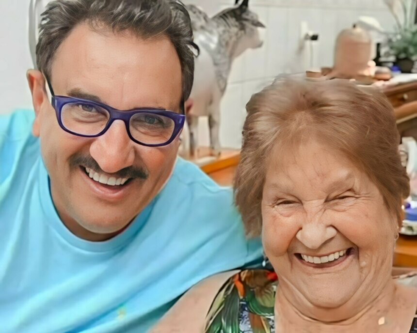Ratinho sorridente ao lado de sua Maria Massa que está sentada em uma cadeira. Os dois estão sorrindo