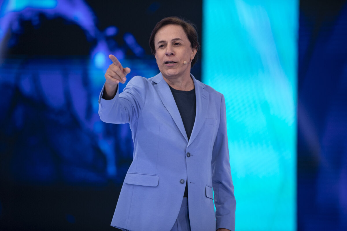 Tom Cavalcante veste terno azul claro está em pé no centro do palco do Acerte ou Caia!