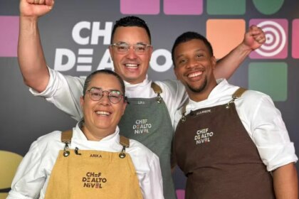 A imagem mostra três finalistas do reality show "Chef de Alto Nível". Da esquerda para a direita, Arika, Lira e Mamede. Os três estão sorrindo e comemorando, com os punhos erguidos. Todos vestem dólmãs brancos e aventais de chef com a inscrição "CHEF DE ALTO NÍVEL". O painel ao fundo repete o nome do programa.