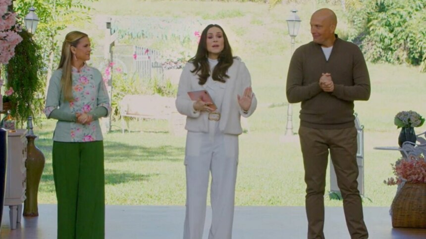 A apresentadora e os jurados do programa 'Bake Off Brasil' estão em um cenário com muita vegetação. Da esquerda para a direita, estão Beca Milano, de blusa verde estampada e calça verde, Nadja Haddad de casaco e calça brancos, e Giuseppe Gerundino de suéter marrom.
