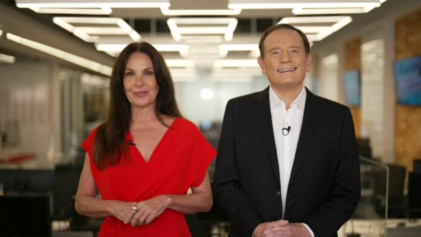 A apresentadora Carolina Ferraz, de vestido vermelho, e o jornalista Roberto Cabrini, de terno preto, estão em um estúdio. Ambos sorriem para a câmera, e o nome do arquivo os associa ao programa 'Domingo Espetacular'.