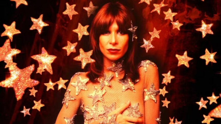 A cantora Rita Lee, com cabelos ruivos, usa uma maquiagem forte e um vestido transparente com estrelas brilhantes. O fundo da foto, que parece ser um poster de documentário, também é vermelho e cheio de estrelas.
