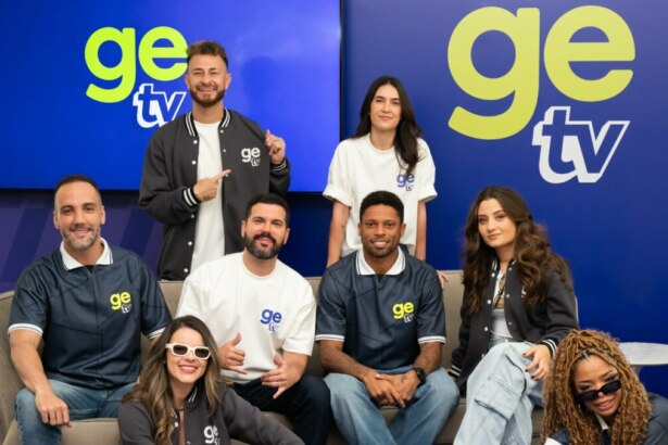 Foto em grupo do elenco da GE TV posando em um estúdio azul. Os oito apresentadores usam roupas casuais e uniformes com a marca, sorrindo para a câmera.