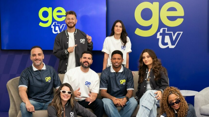 Foto em grupo do elenco da GE TV posando em um estúdio azul. Os oito apresentadores usam roupas casuais e uniformes com a marca, sorrindo para a câmera.