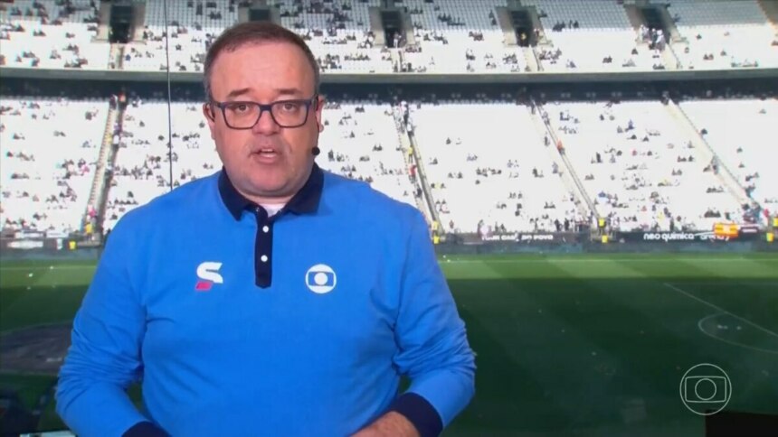 Everaldo Marques, narrador esportivo, aparece em um estúdio com o fundo da Neo Química Arena lotada. Ele usa óculos e uma camisa polo azul com o logo da Globo Esporte.