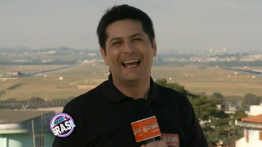 O repórter Humberto Ascencio, sorrindo e segurando um microfone em um ambiente externo. Ele está em um terraço com um fundo desfocado que mostra uma paisagem urbana com um campo e uma pista de aeroporto. Na parte inferior da tela, um logo do programa "O Melhor do Brasil" é visível.