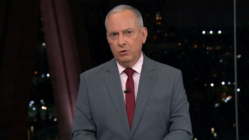 O jornalista José Roberto Burnier, usando um terno cinza, camisa rosa clara e gravata vermelha, apresenta o jornal. Ele olha seriamente para a câmera, com um fundo desfocado que mostra o cenário do telejornal "SP2" e as luzes de uma cidade à noite.