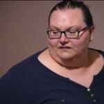 Lindsey de blusa azul, extremamente obesa, com 294 quilos, olhando para o lado e de óculos de grau