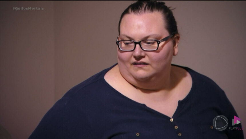 Lindsey de blusa azul, extremamente obesa, com 294 quilos, olhando para o lado e de óculos de grau