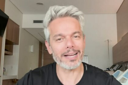 Otaviano Costa, com cabelo grisalho e barba, sorri em um quarto de hospital, após ser afastado do Melhor da Noite