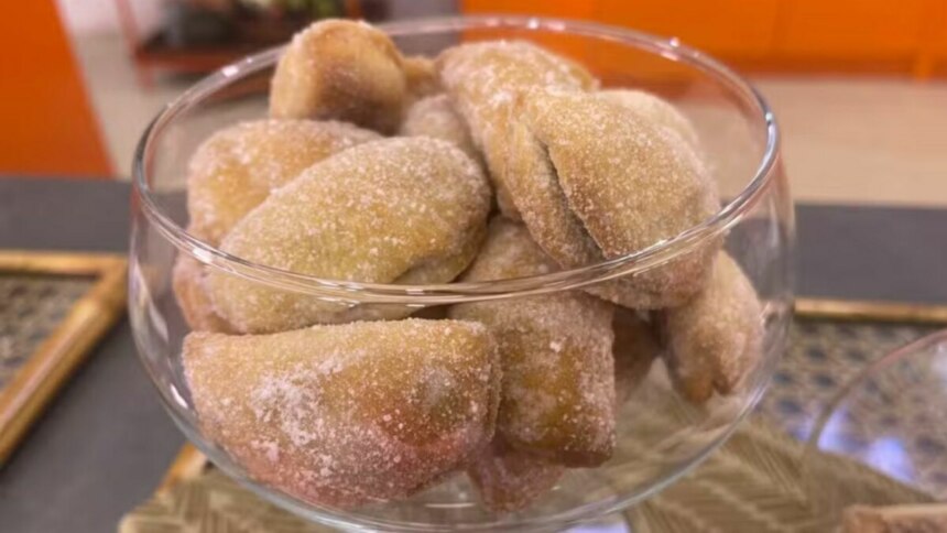 Um close-up de uma taça de vidro cheia de pastéis de nozes. Os pastéis são pequenos, ovais e polvilhados com açúcar. A imagem, com o nome do arquivo, é de uma receita do programa 'Mais Você'.