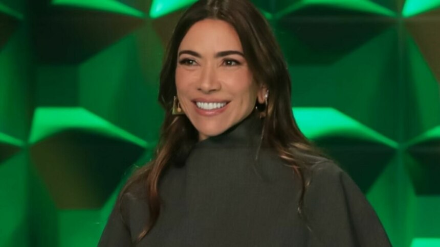 A apresentadora Patricia Abravanel, em um close-up, sorri levemente e olha para a frente. Ela usa uma blusa preta de gola alta e brincos grandes e dourados. O fundo é um cenário de estúdio com painéis verdes e triangulares. O nome do arquivo a associa ao 'Show do Milhão Celebridades'.