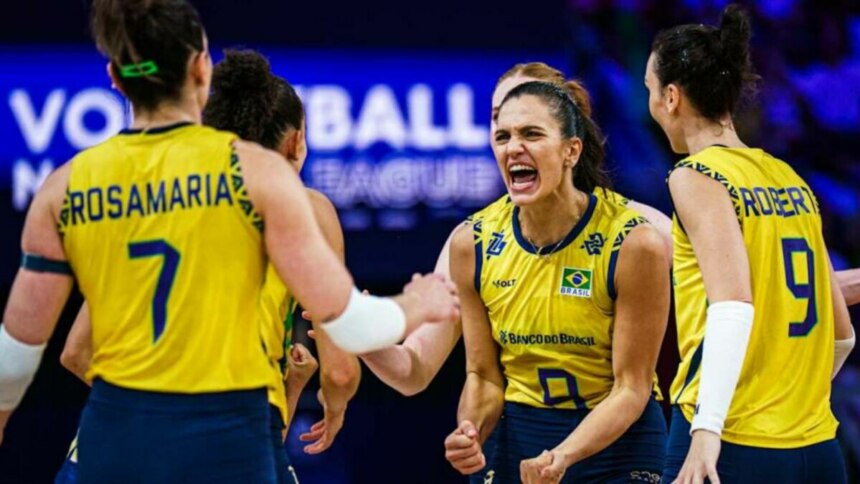 A imagem mostra a jogadora de vôlei Gabi Guimarães, com uma expressão de comemoração, em meio às suas colegas de equipe da Seleção Brasileira. Gabi está vestindo a camisa amarela com detalhes azuis. Ao fundo, uma placa com a inscrição "VOLLEYBALL LEAGUE". As jogadoras Rosamaria e Roberta, com as camisas 7 e 9, respectivamente, também são visíveis na imagem.
