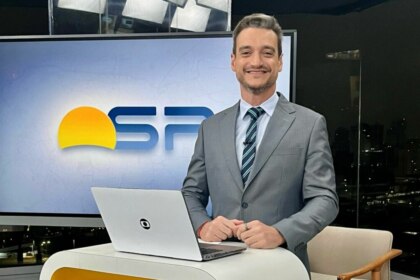 Tiago Scheuer sorridente em frente ao telão no cenário do Bom Dia SP