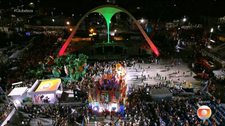 Imagem aérea noturna do Sambódromo do Rio de Janeiro durante um desfile de carnaval. A passarela está cheia de passistas e alegorias de uma escola de samba. As arquibancadas estão repletas de público. O icônico arco central está iluminado em vermelho e verde. A hashtag "#Globeleza" e o logo da Globo com a indicação "AO VIVO" são visíveis