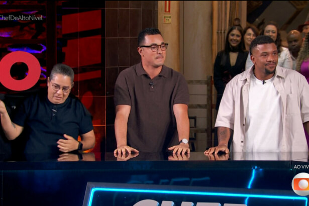 Três finalistas do reality "Chef de Alto Nível" — Luiz Lira, Arika Messa e Allan Mamede — estão lado a lado atrás de um balcão, sorrindo e aplaudindo durante a transmissão ao vivo da grande final