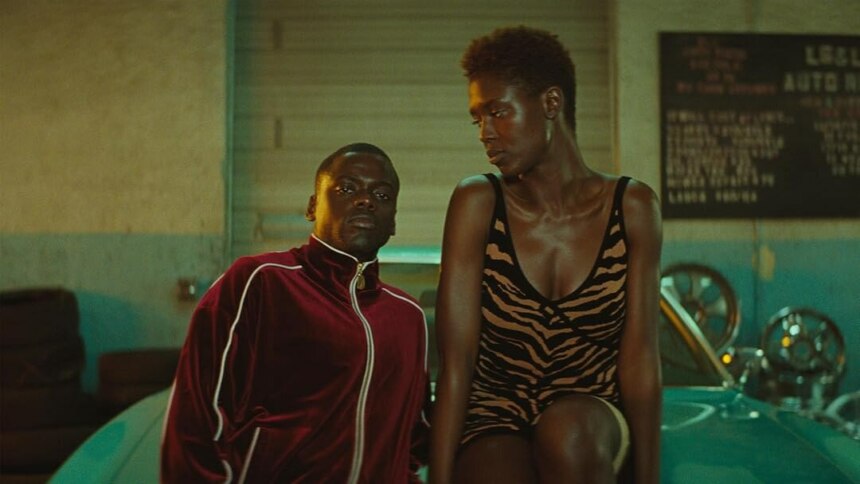 Os atores Daniel Kaluuya e Jodie Turner-Smith, como Queen e Slim, lado a lado em uma cena do filme Queen & Slim, com o ator usando um agasalho de veludo vinho e a atriz vestindo um minivestido com estampa de animal