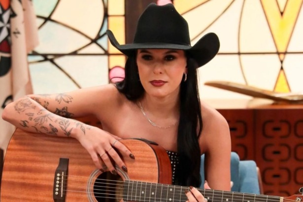 Ana Castela de chapéu e tocando violão em trecho da novela A Caverna Encantada