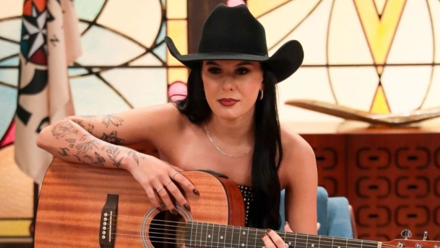 Ana Castela de chapéu e tocando violão em trecho da novela A Caverna Encantada