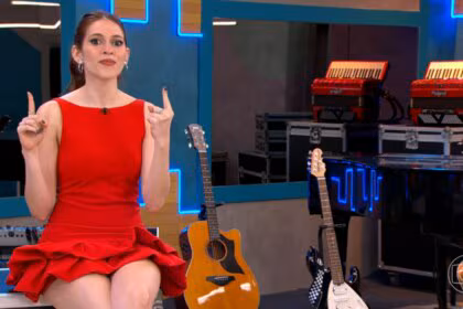 Ana Clara, de vestido vermelho, em um estúdio musical com guitarras e acordeões ao fundo no Estrela da Casa
