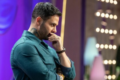Diego Lozano, de camisa verde-azulada e com tatuagens visíveis no pescoço e braço, olhando pensativo para o lado com a mão no queixo, no cenário de MasterChef Confeitaria.