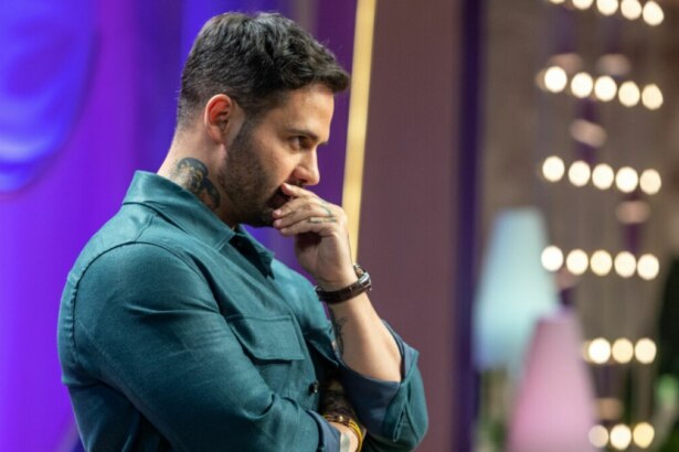 Diego Lozano, de camisa verde-azulada e com tatuagens visíveis no pescoço e braço, olhando pensativo para o lado com a mão no queixo, no cenário de MasterChef Confeitaria.