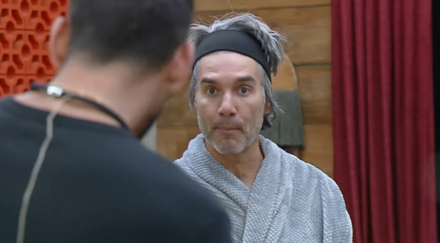 Fernando Sampaio, de roupão cinza e tiara, olha fixamente para outro participante, Nizam, durante uma discussão em A Fazenda.