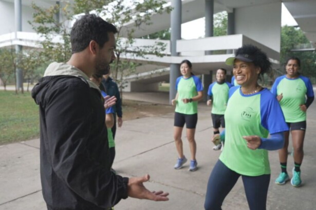 Reportagem do Globo Repórter sobre corrida: uma mulher sorri, correndo com camisa verde e azul, enquanto um homem a entrevista em um parque.
