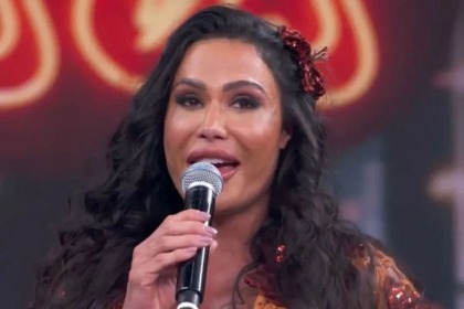 A musa fitness Gracyanne Barbosa chorando, segurando um microfone e com uma flor vermelha no cabelo, no palco do quadro Dança dos Famosos.