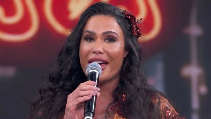 A musa fitness Gracyanne Barbosa chorando, segurando um microfone e com uma flor vermelha no cabelo, no palco do quadro Dança dos Famosos.
