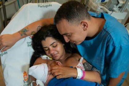 João Gomes e Ary Mirelle, emocionados, segurando o bebê recém-nascido no colo de Ary em um quarto de hospital.