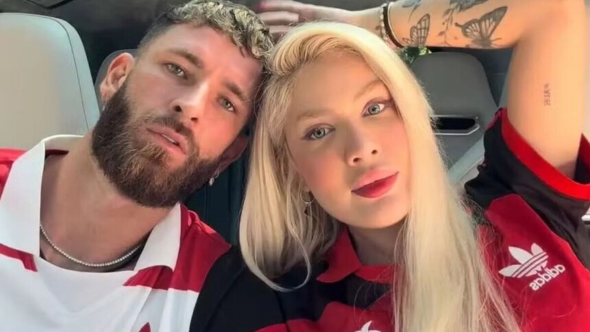O jogador Léo Pereira, de barba, e a influenciadora Karoline Lima, de cabelo loiro, posam lado a lado em uma selfie. Ambos usam camisas do Flamengo.