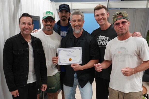 O apresentador Marcos Mion (centro) posa sorrindo com os cinco integrantes do Backstreet Boys no Caldeirão, segurando um certificado.