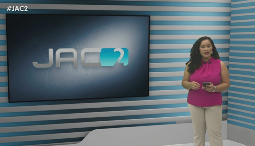 Quésia Melo em frente ao televisor no cenário do Jornal do Acre