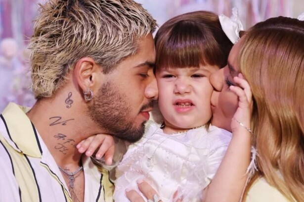 O cantor Zé Felipe, com cabelos descoloridos, beija a cabeça da filha Maria Flor, que está com uma expressão engraçada. A influenciadora Virginia Fonseca beija o rosto da filha ao lado deles em uma foto de família.