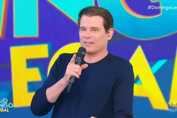 Celso Portiolli segura microfone do Domingo Legal e sorrir no palco do programa