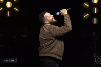 Janício segura o microfone como se fosse cantar no palco do Estrela da Casa 2