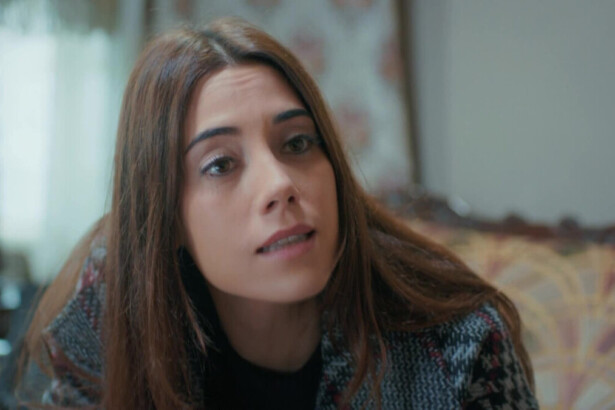 Cansu Dere sorridente, sentada em um sofá, em cena da novela turca Mãe