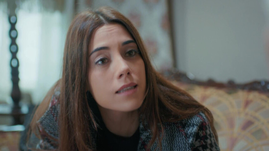 Cansu Dere sorridente, sentada em um sofá, em cena da novela turca Mãe