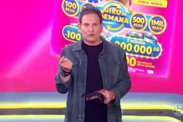 Luis Ricardo no estúdio rosa apresentando a edição 71 da Tele Sena Semanal. Ele segura o bilhete da edição